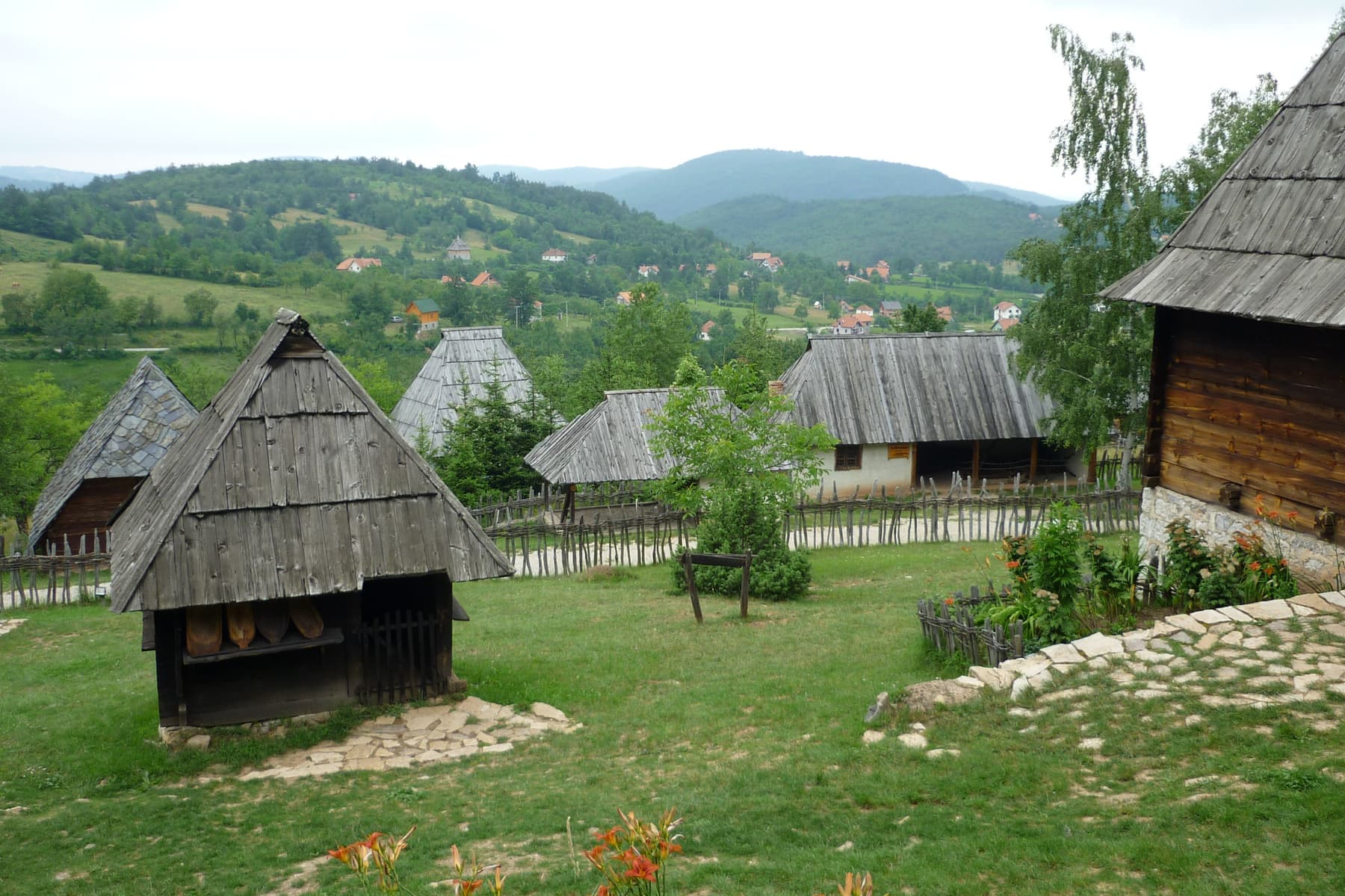 Drvene brvnare sa šindrom u muzeju Staro selo u Sirogojnu, sa selom u pozadini